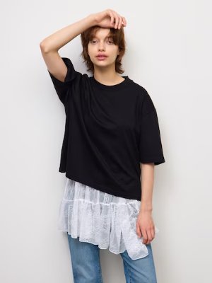 Model wearing a black tunic showing a white lace asymmetrical hem over jeans.