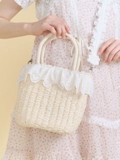 Model holding a cream lace-frill basket bag with double handles against a pale background.