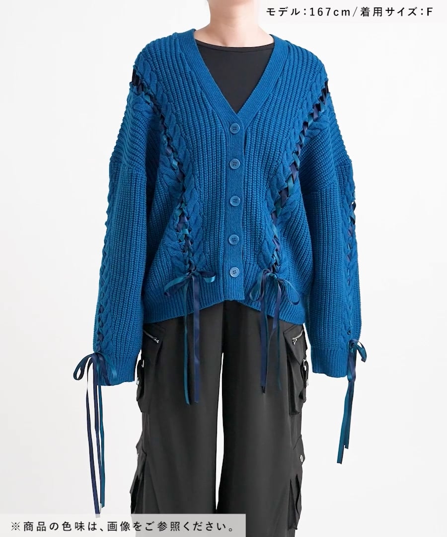 Front view of a blue lace-up mid cardigan worn by a model over a black top and dark pants.