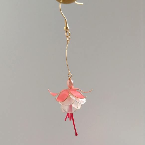 A single dangling fuchsia plastic earring with a gold hook photographed on a neutral background.
