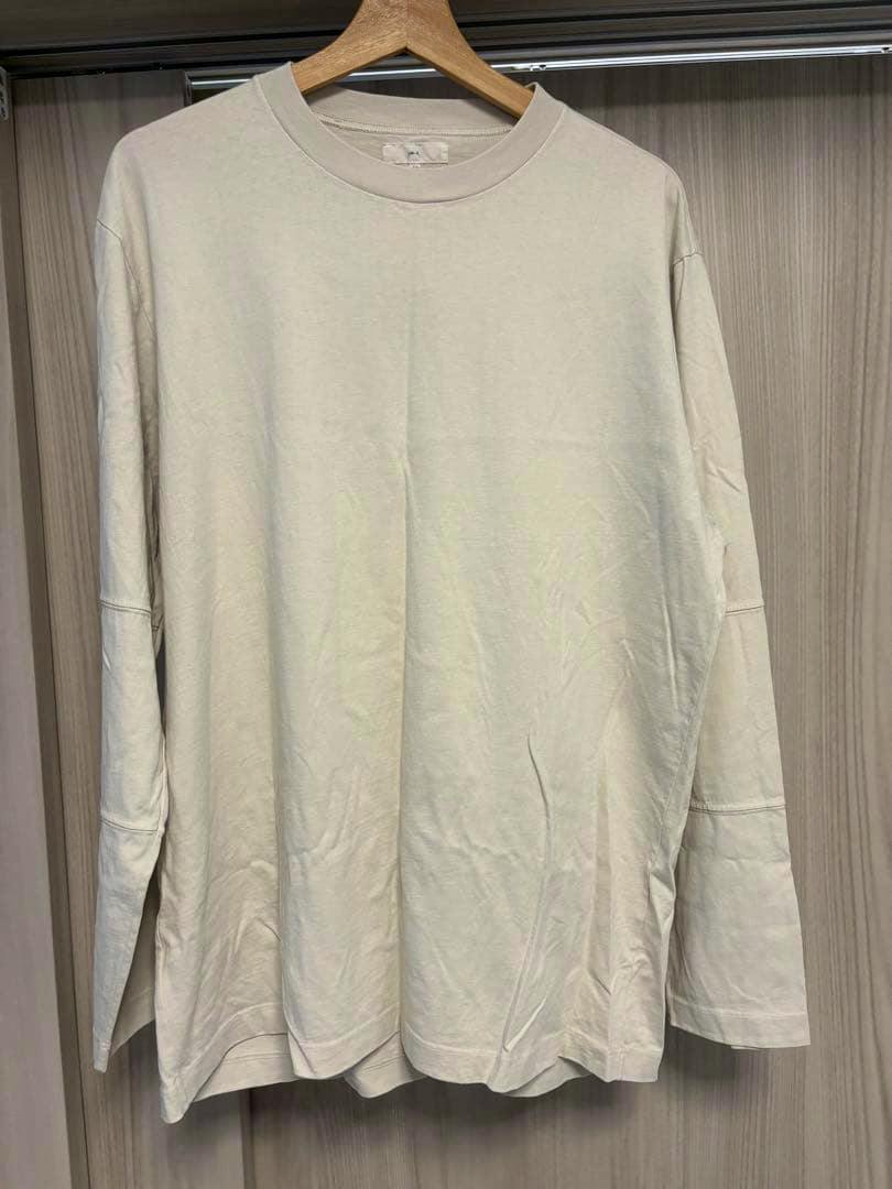 Front view of a light-colored men's long-sleeve cotton T-shirt hanging on a wooden hanger against a wooden background.