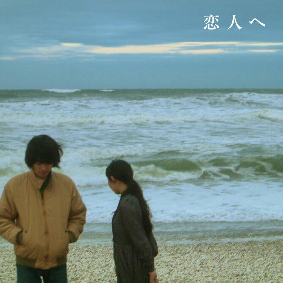 CD cover art showing two people on a pebbled beach with waves behind and the Japanese title 『恋人へ』 at the top.