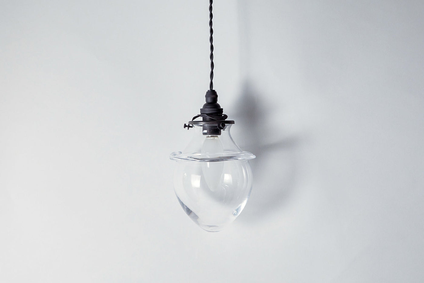 A clear glass lampshade with a black lampholder suspended against a white background.