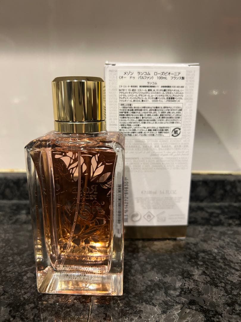 Glass 100ml Maison Lancôme Rose Peonia perfume bottle with its box behind it on a countertop.