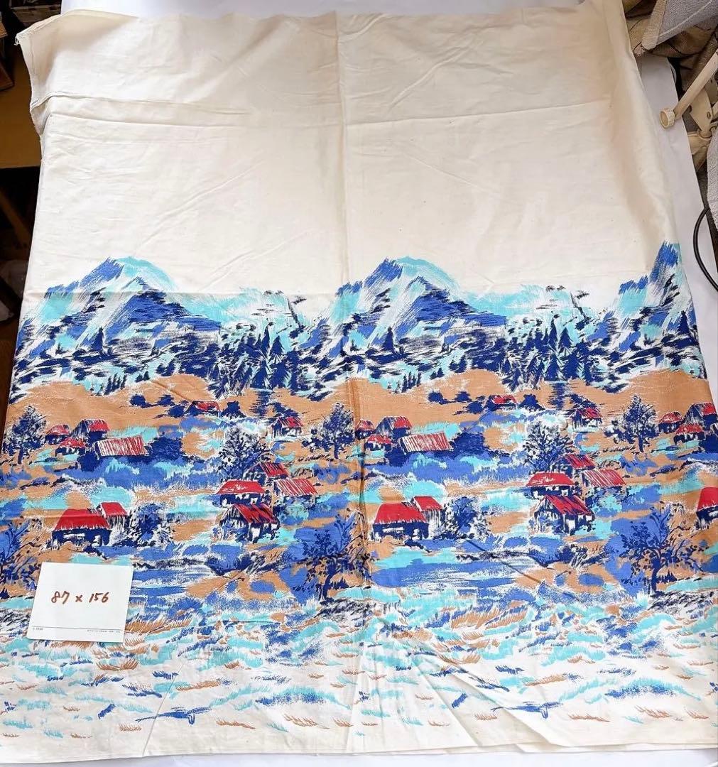A rectangular cotton fabric piece laid flat showing a blue and orange landscape print and a small note reading 87×156.