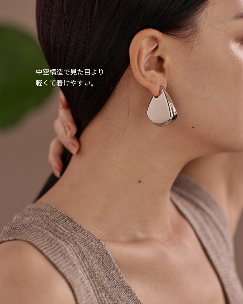 Close-up of a model wearing a large silver-toned earring on her ear.