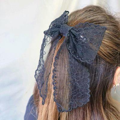 Black organza lace ribbon barrette clipped to the back of a woman's hair with long scalloped tails visible.