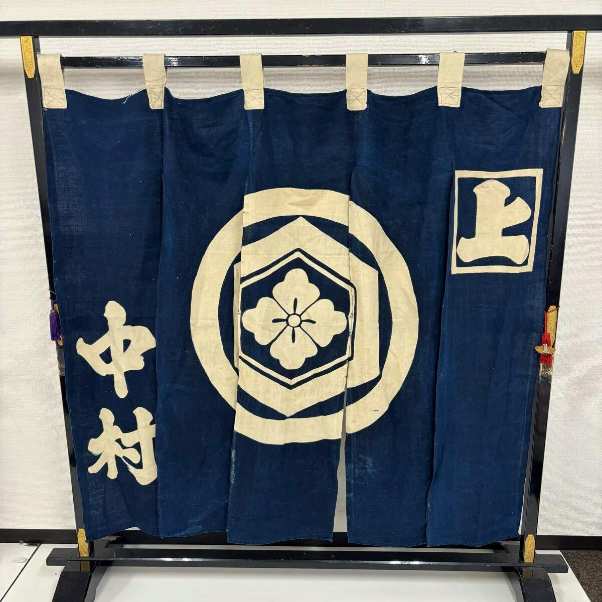 Indigo-dyed cotton noren curtain with a white circular crest and kanji characters hanging on a display frame.