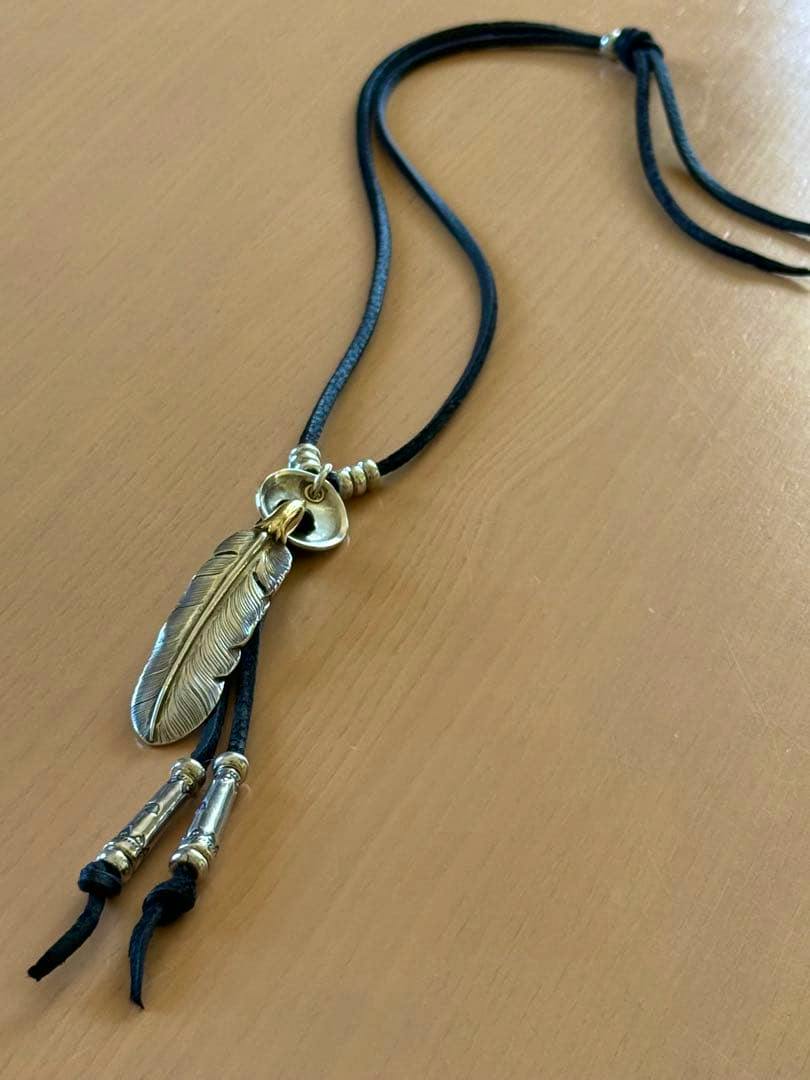 Deerskin lace necklace with a feather pendant, eagle-head and metal bead accents laid on a wooden surface.