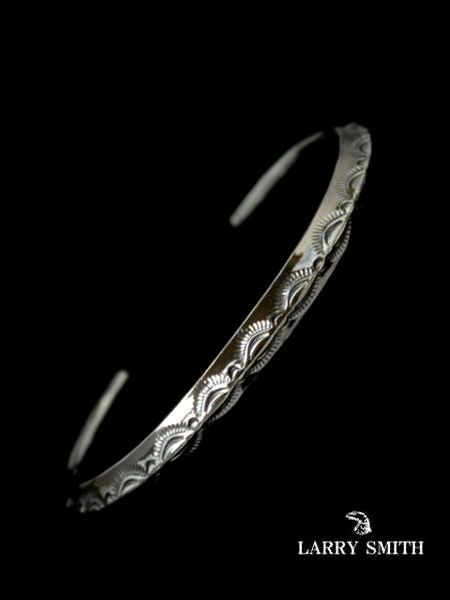 Silver men's thin triangle bracelet with leaf-pattern engraving on a black background.