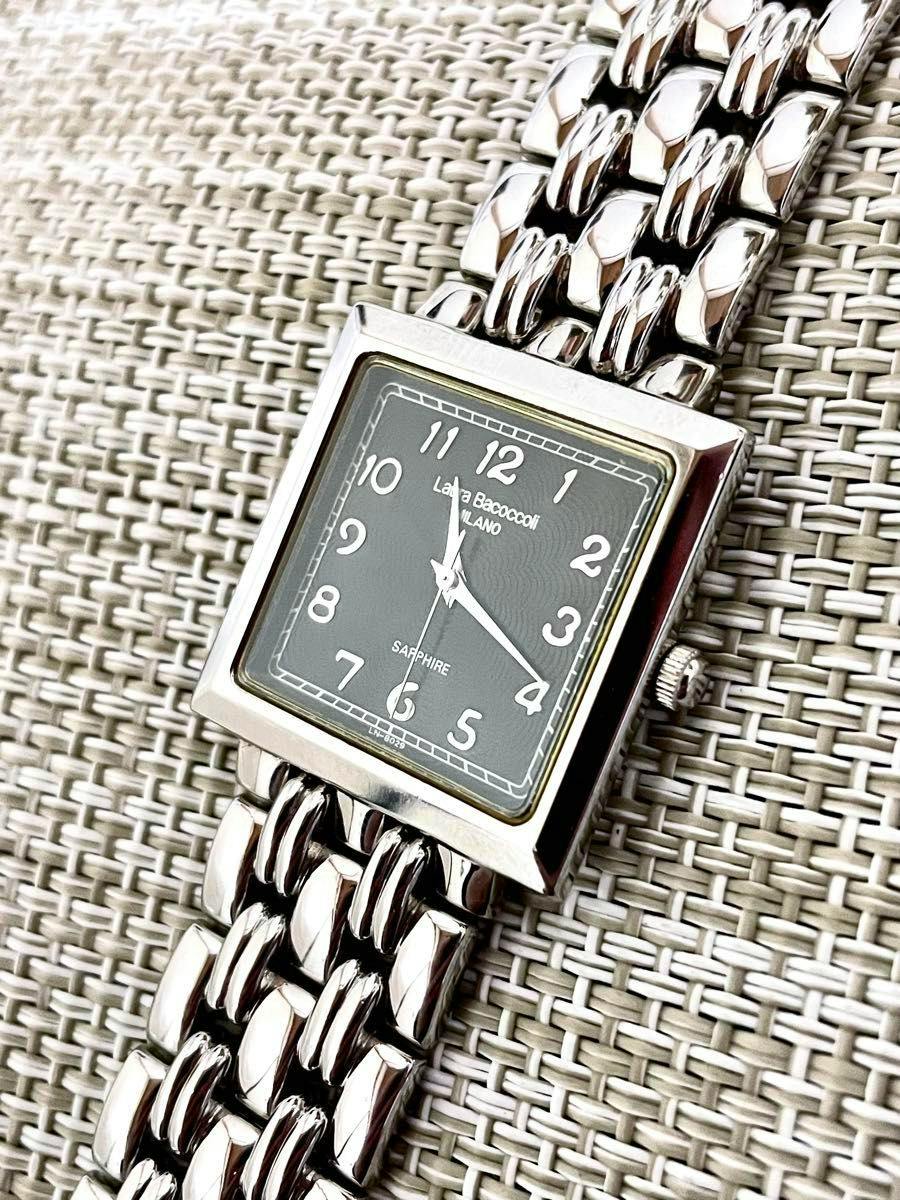 Square Laura Bacoccoli Milano wristwatch with a black dial labeled "SAPPHIRE" on a metal link bracelet placed on a woven surface.