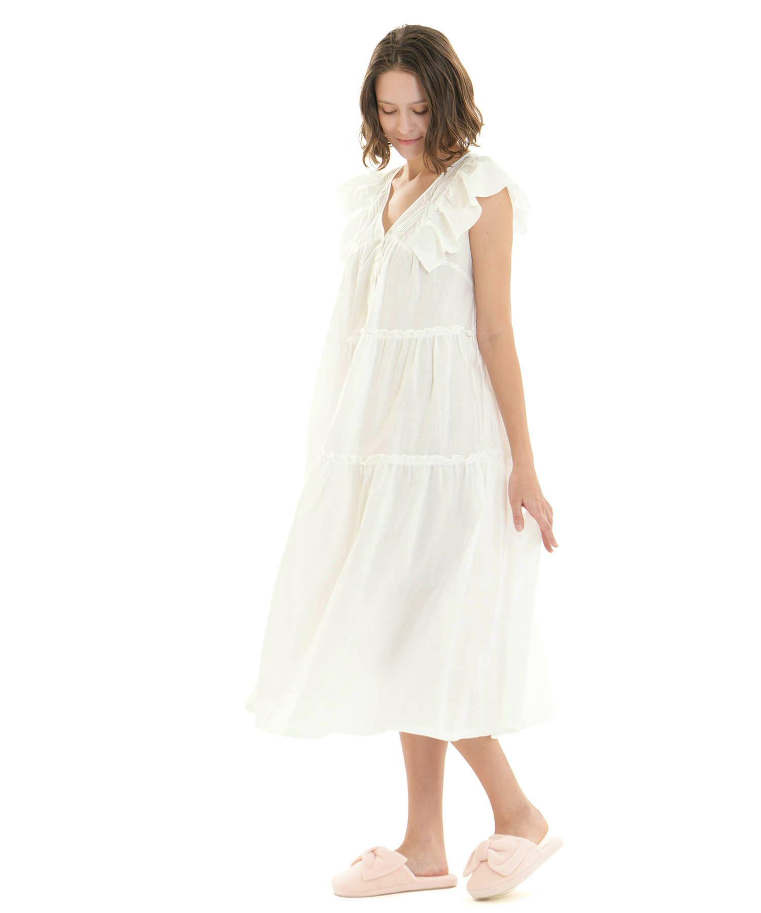 A model wearing a white cotton frill dress with a V-neck, ruffled sleeves, and tiered skirt.