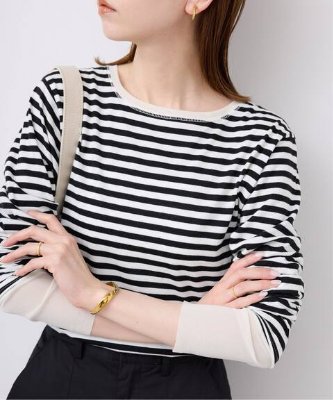 Woman wearing a black-and-white striped layered-sleeve long-sleeve tee shown from the chest up.
