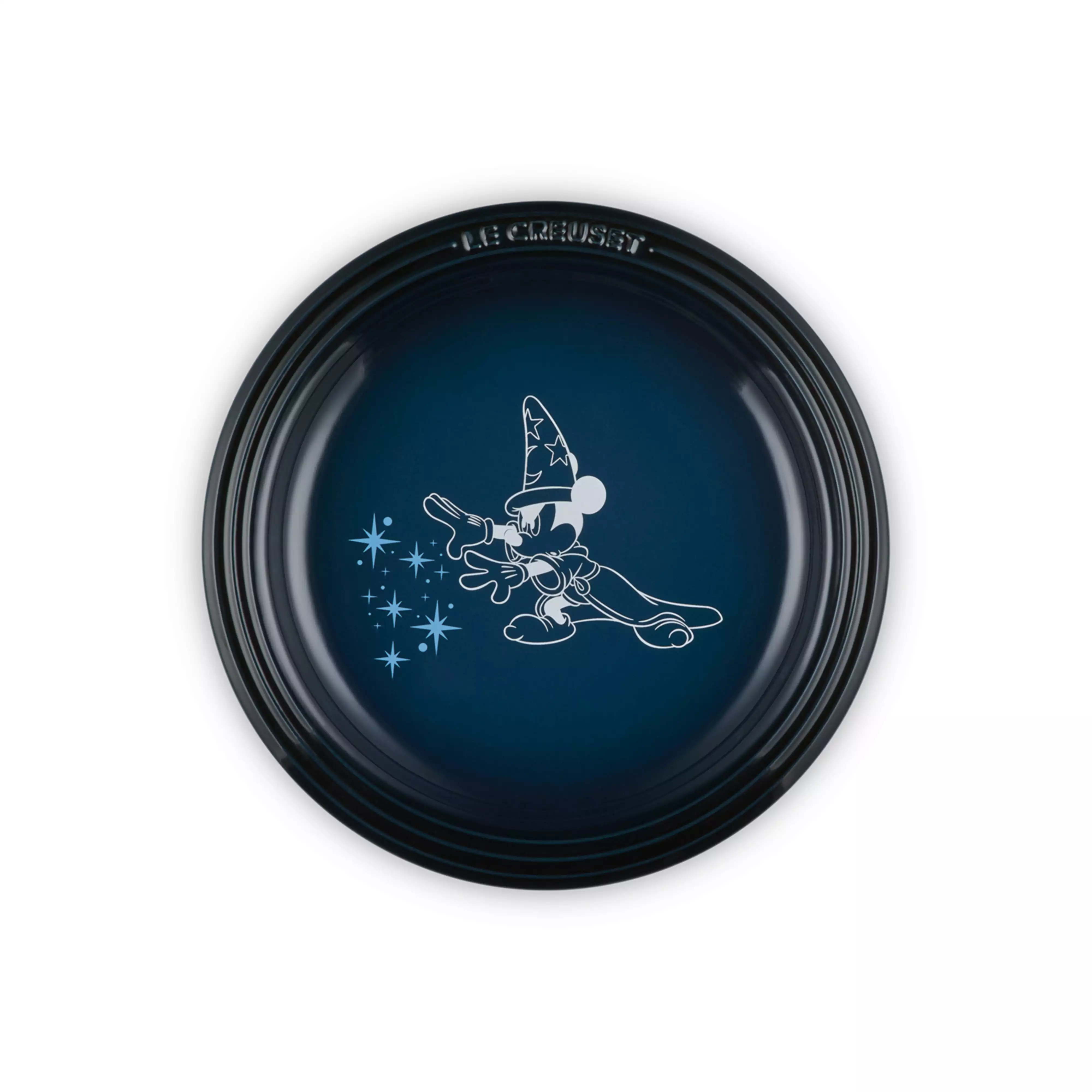 Top-down photograph of a Le Creuset porcelain plate in dark blue with a white outline illustration of Sorcerer Mickey in the center.