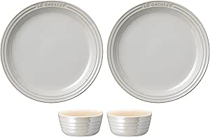 Two round white Le Creuset plates with two matching small white ramekins shown on a white background.