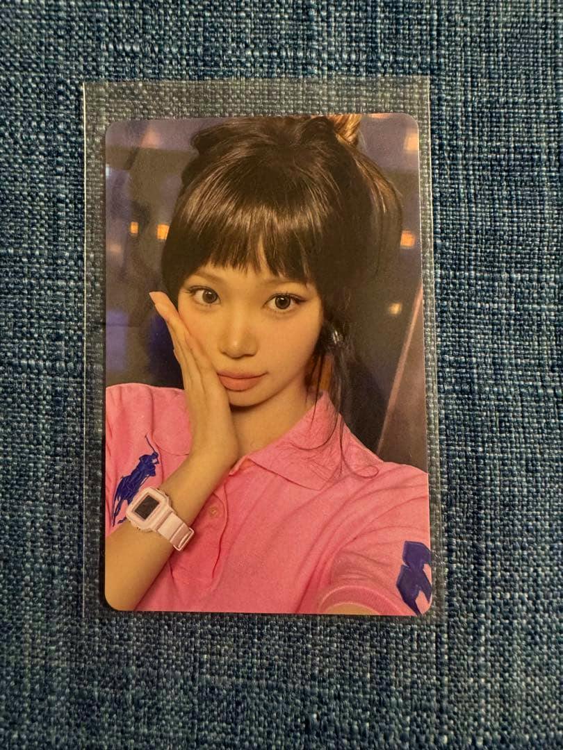 A photocard in a clear sleeve showing a portrait-style image of the card placed on a blue textured fabric background.