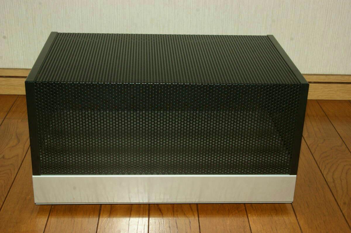 Front view of the amplifier's perforated black bonnet mounted on a silver aluminum chassis sitting on a wooden floor.