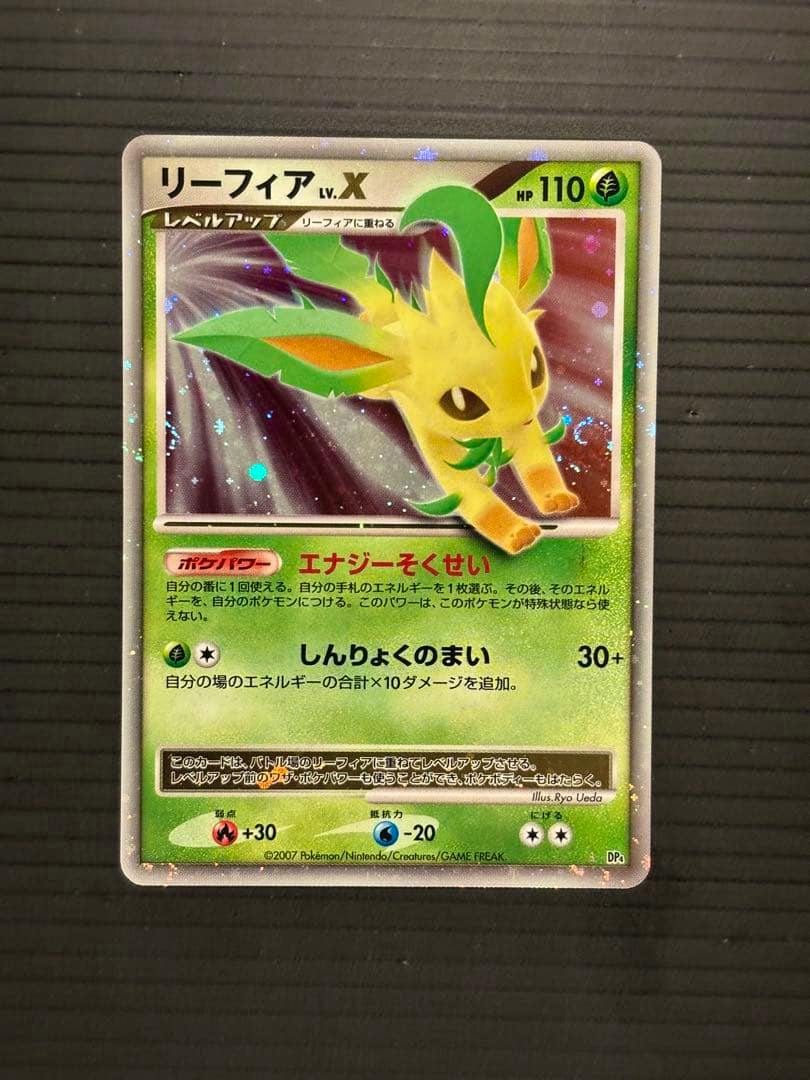 Photo of the front of a holographic Japanese Leafeon (リーフィア) Pokémon trading card on a black textured background.