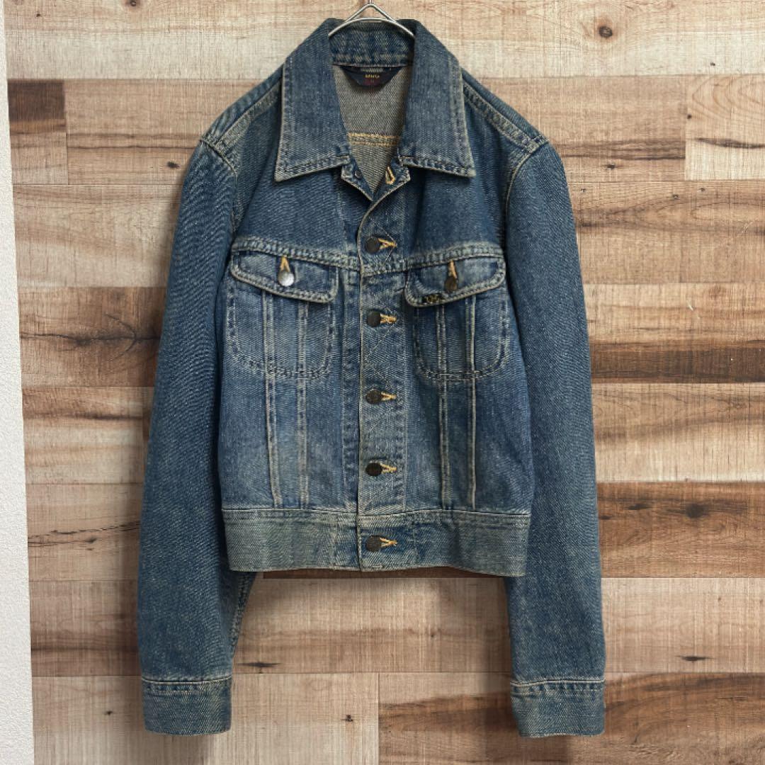 Front view of a Lee men's blue denim jacket with double chest pockets hanging on a hanger against a wooden background.