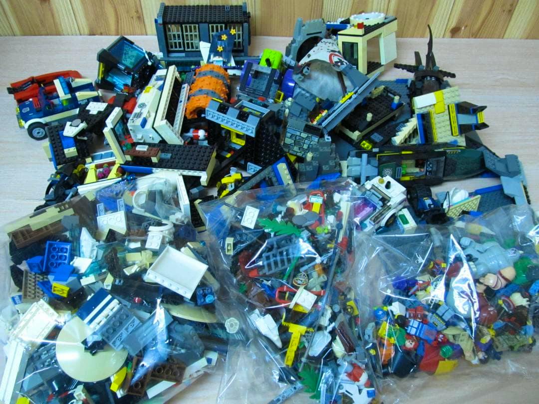Pile of assorted LEGO bricks, assembled elements, and several clear plastic bags of small parts on a wooden table.