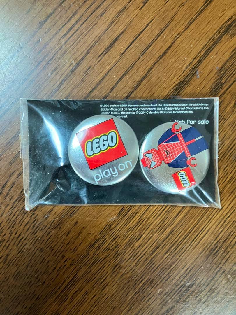 Two LEGO Spider-Man tin badges in their original plastic packaging on a wooden surface.