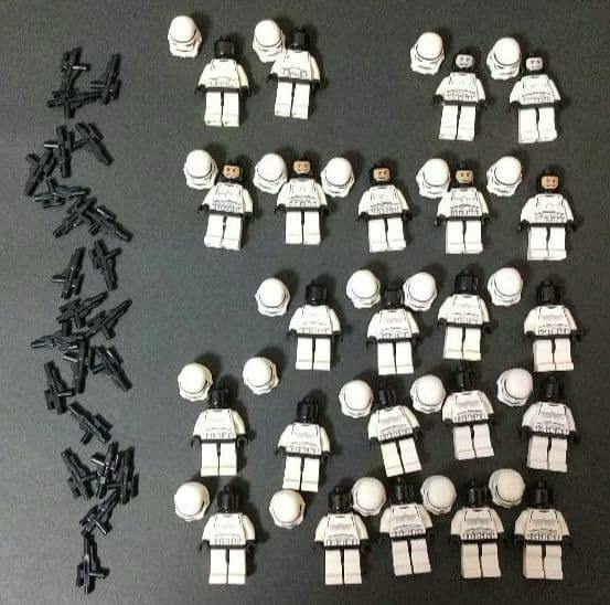 Many LEGO Star Wars stormtrooper minifigure parts and small black blaster accessories arranged on a black surface.