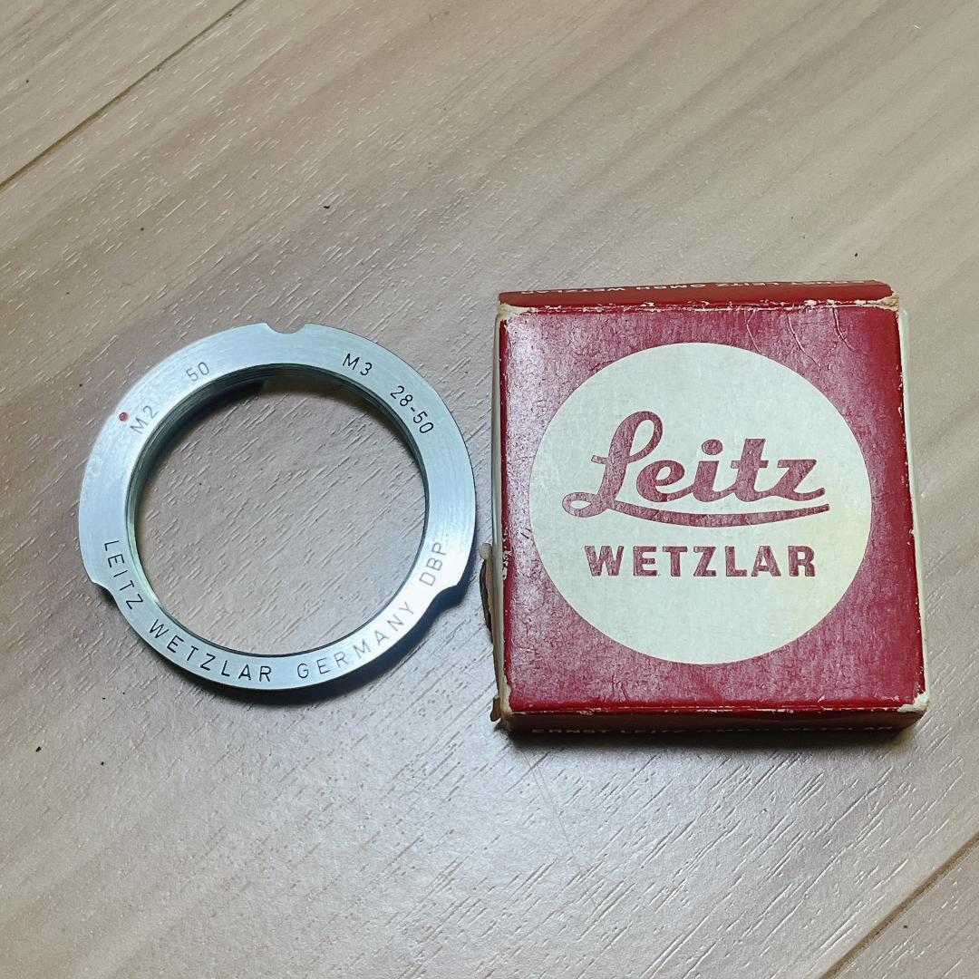 Camera mount adapter ring shown next to a Leitz Wetzlar box on a wooden surface.