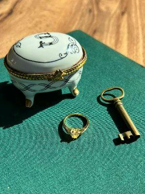 A LEMON HEART RING (gold-tone ring with a yellow heart-shaped stone) placed on green fabric beside a small decorative trinket box and a vintage-style key.