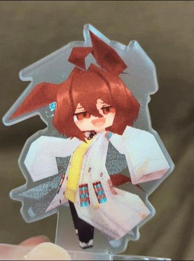 Hand holding a lenticular acrylic stand showing a stylized Agnes Tachyon character.