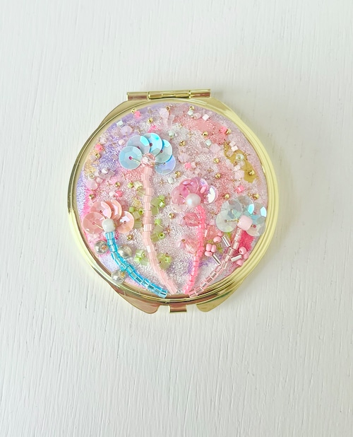 Round compact mirror with a pink glittery top decorated with sequins and beads, shown on a white background.