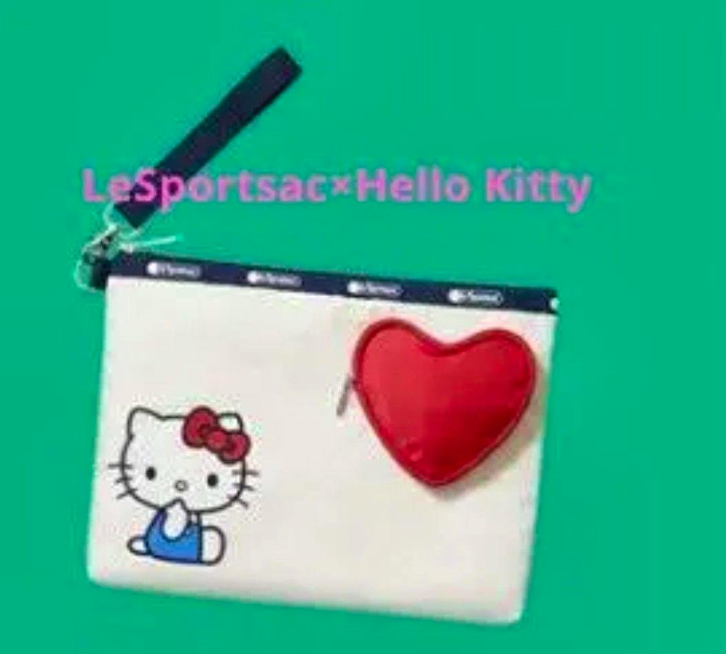 White canvas LeSportsac × Hello Kitty pouch with a printed Hello Kitty design and an attached red heart charm shown against a green background.