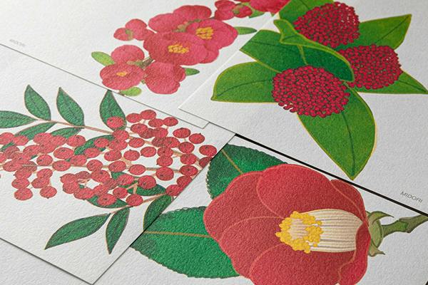 Close-up photo of letter pad sheets showing four red winter floral designs printed on textured paper.
