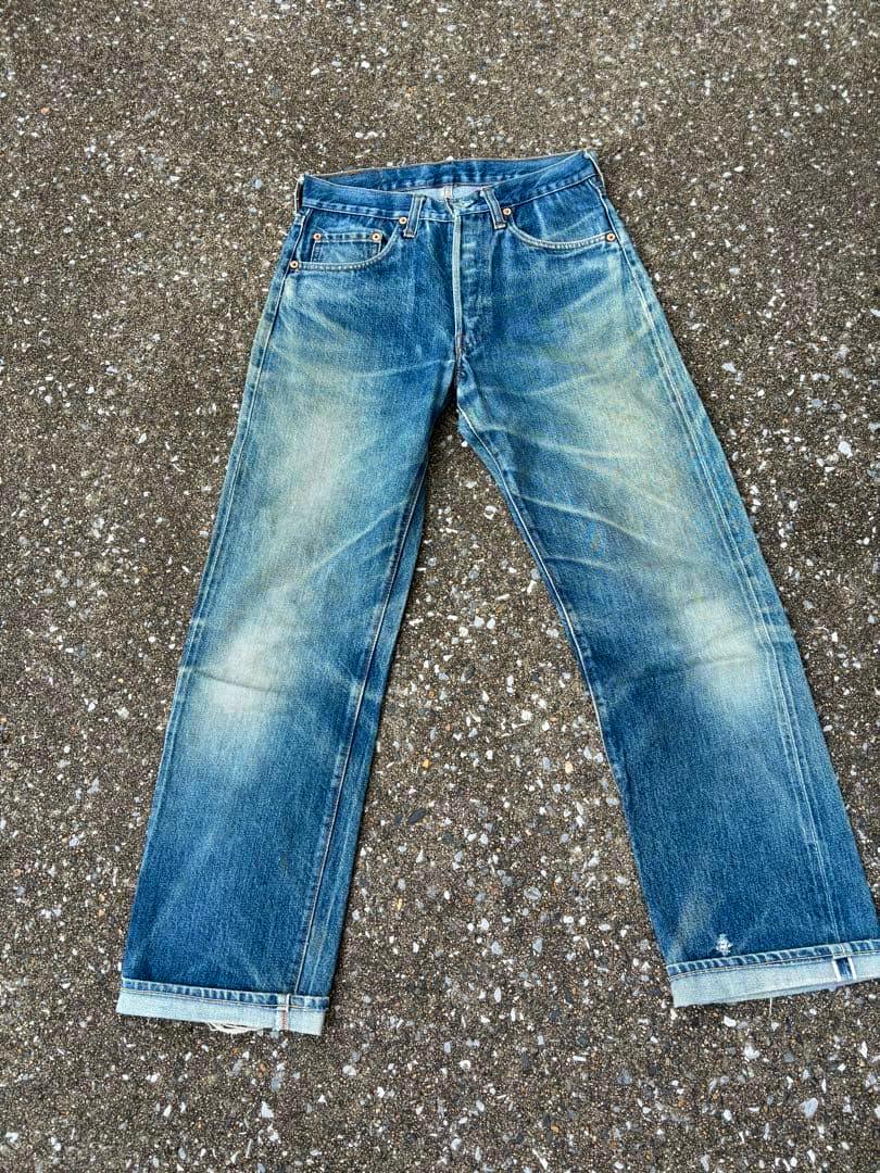Front view of Levi's 501 men's blue denim jeans laid flat on a gravel surface showing faded whiskering and rolled cuffs.