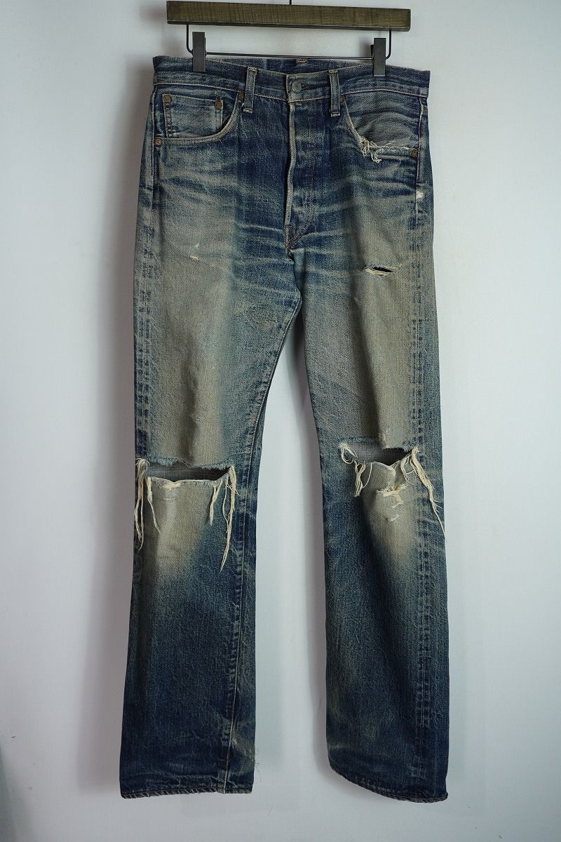 Front view of Levi's 501 blue denim jeans with ripped knees hanging on a hanger.