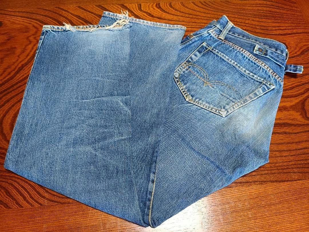 Men's cotton jeans laid flat on a wood surface showing the back pocket, belt loop, and frayed hem.