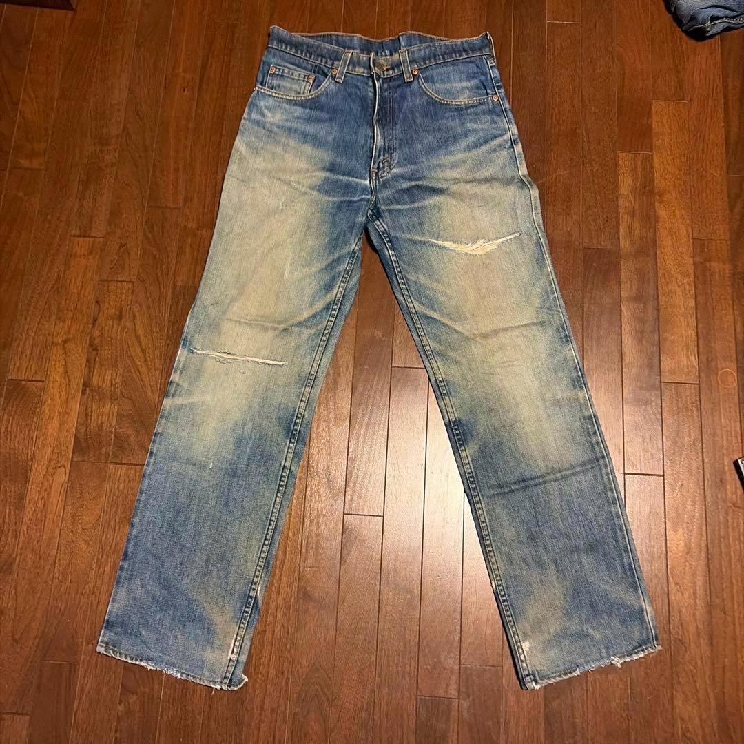 Front view of the Levi's men's jeans laid flat on a wooden floor, showing faded wash, knee distressing, and frayed hems.