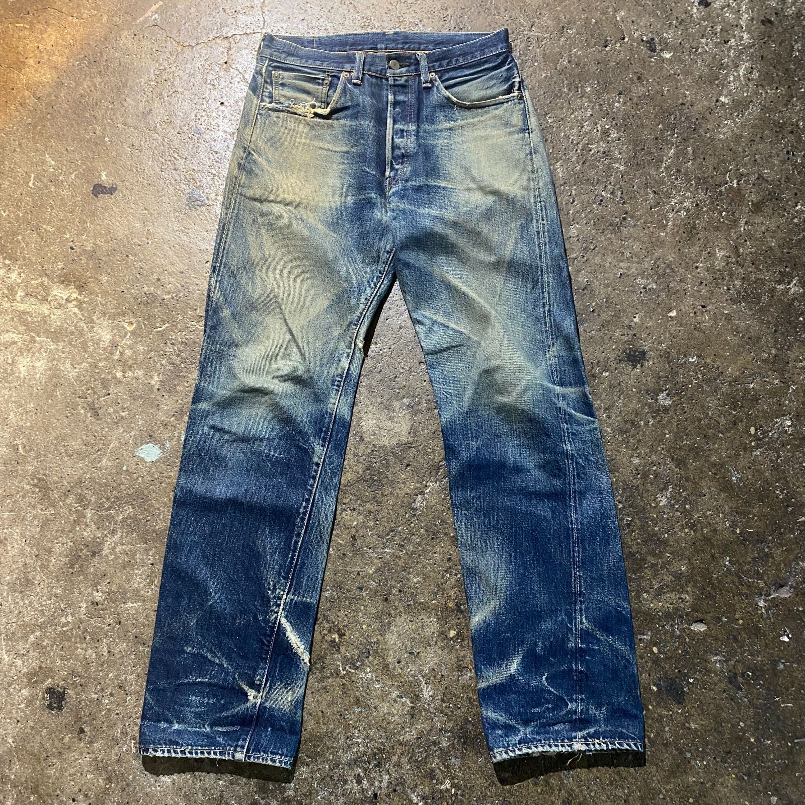 LEVI'S men's blue denim jeans laid flat on a concrete floor, front view showing fades and wear.
