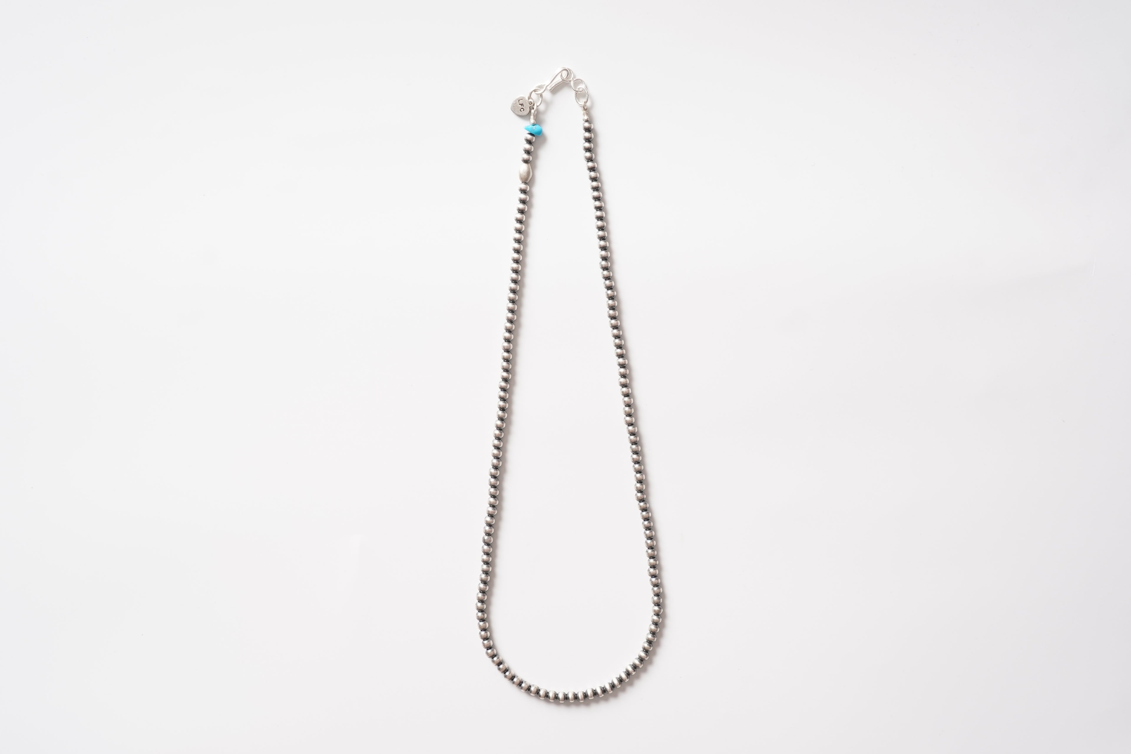 Full view of the LFC silver bead necklace with a Sleeping Beauty turquoise accent laid on a white background.