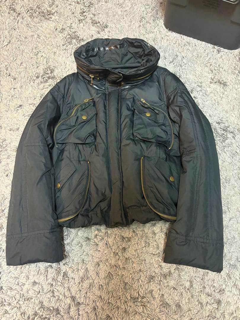 Front view of a black men's down jacket with multiple zippered pockets laid flat on a carpet.