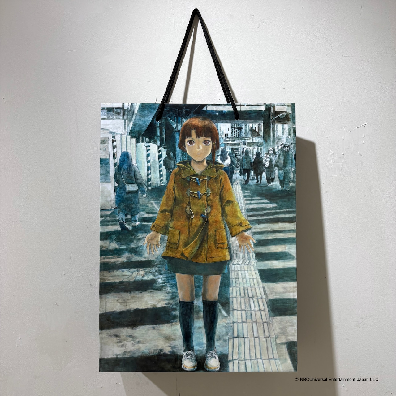 Photograph of a paper shopper bag with black handles featuring an illustration of a girl standing on a crosswalk.