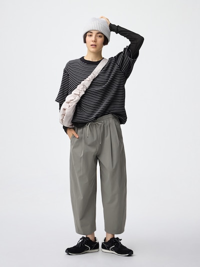 Model wearing light denim barrel ankle men's pants in gray, shown full-length with a striped top and sneakers.