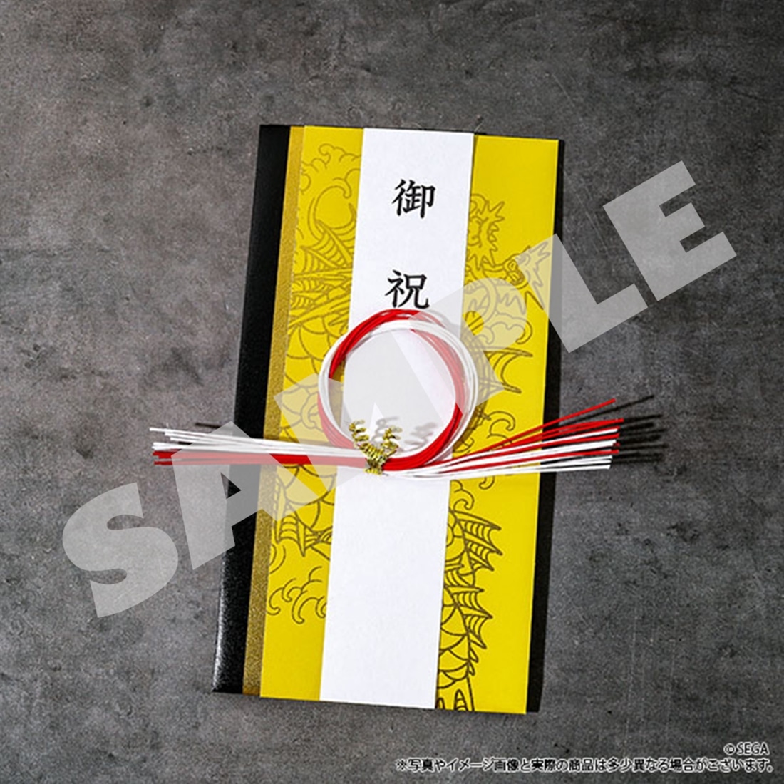 Yellow celebration money envelope (goshugi-bukuro) with a white vertical strip reading 「御祝」, a red-and-white mizuhiki knot, and a faint dragon pattern.