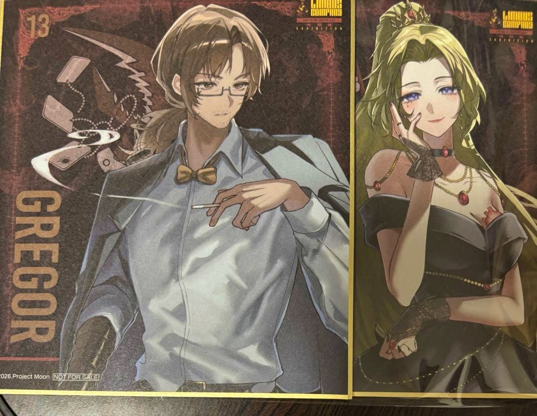 Photograph of a picture board (色紙) depicting two illustrations: a bespectacled man labeled "GREGOR" on the left and a woman in a black dress on the right.