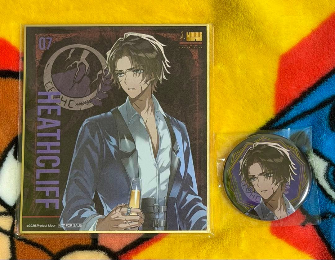Square illustrated shikishi of Heathcliff and a round sealed can badge featuring the same character on a yellow patterned blanket.