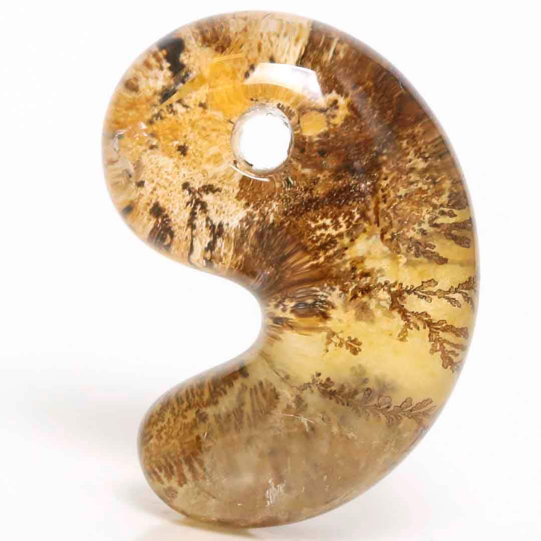 Close-up of a dendritic quartz Izumo-style magatama pendant showing brown and yellow dendritic inclusions and a drilled hole.