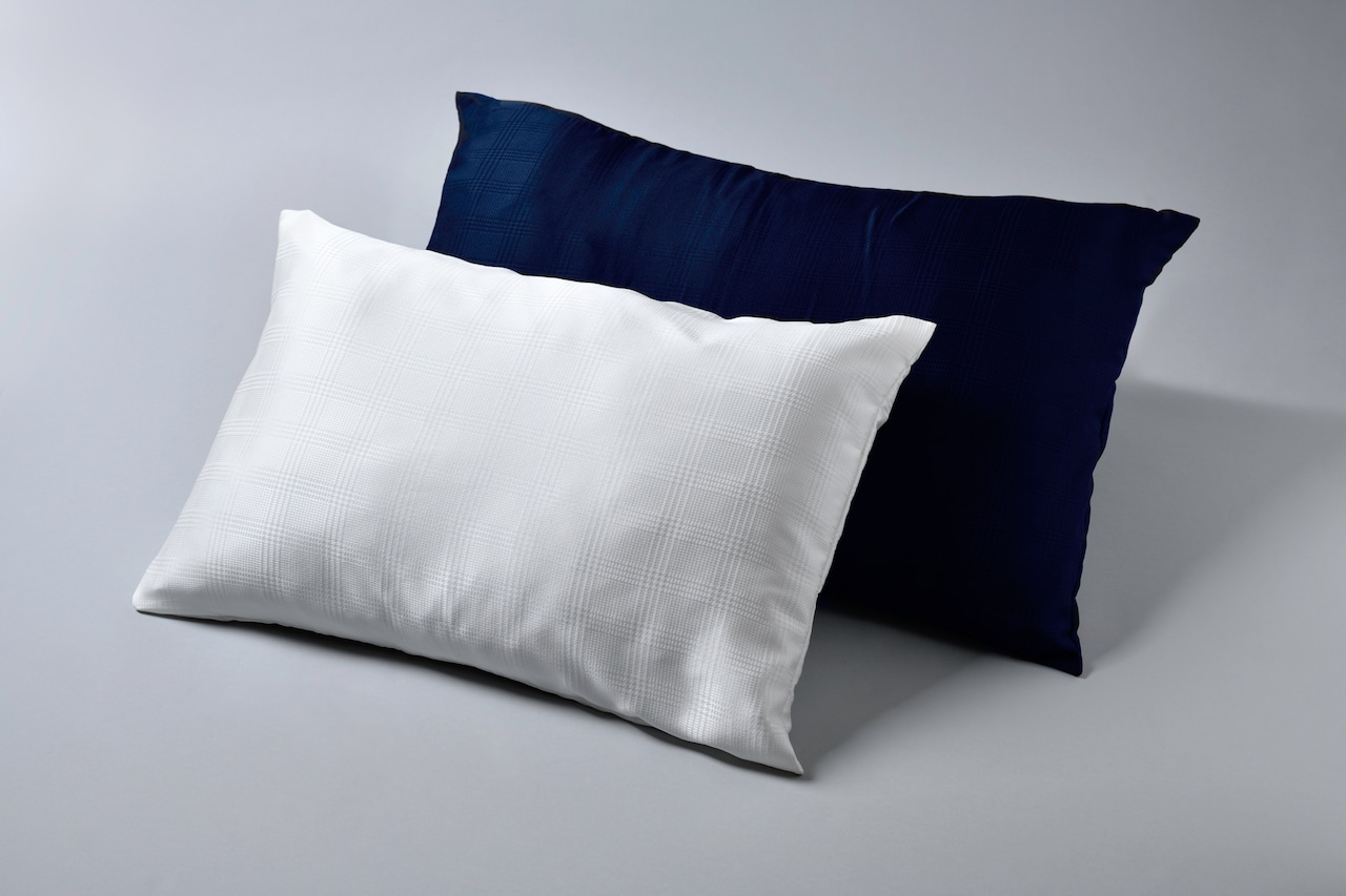 Two silk pillow covers displayed on pillows, one white in front and one dark navy behind.