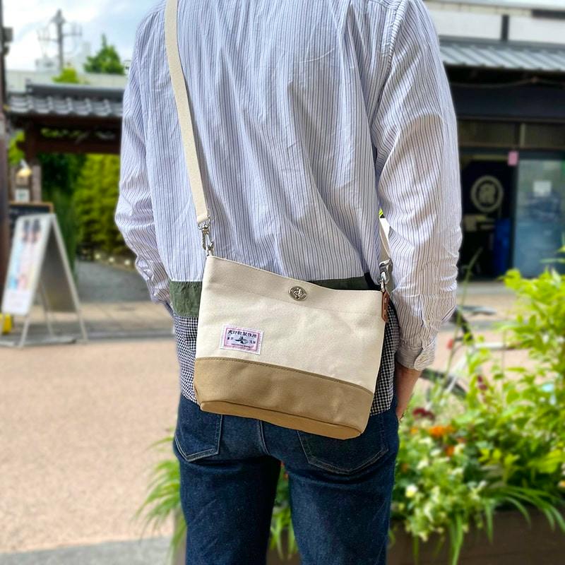 A person wearing a natural-colored cotton mini shoulder bag with a tan lower panel, shown from the back.