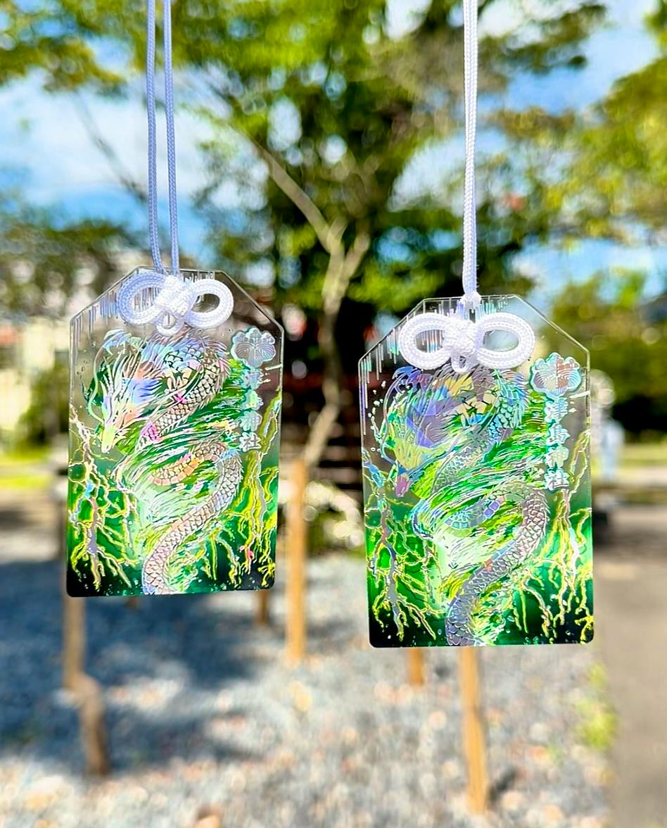 Two holographic dragon amulets with white cords hanging outdoors.