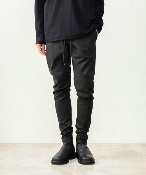 Front view of a model wearing dark men's rubber stretch twill three-dimensional pants from mid-torso to shoes.