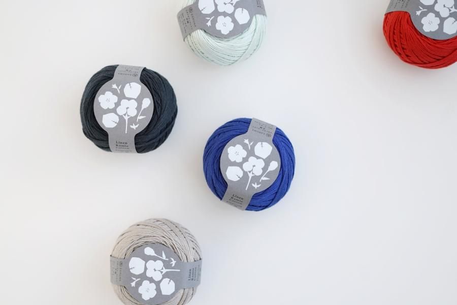 Several wound balls of Linen Ramie Cotton Fingering yarn in different colors with labels on a white background.